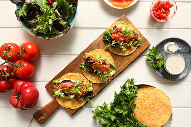 De dessus planche à découper en bois avec de savoureux tacos végétariens placés sur la table blanche — Photo de stock