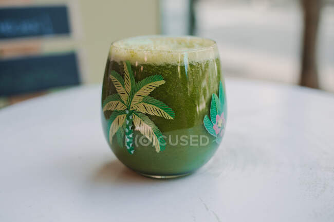 Bubble frothy tasty fragrant green smoothie in glass on wooden table — Stock Photo