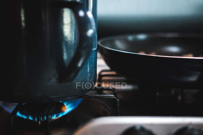 Крупним планом великий металевий кухоль і сковорідку поміщають у вогонь газової плити на кухні — стокове фото