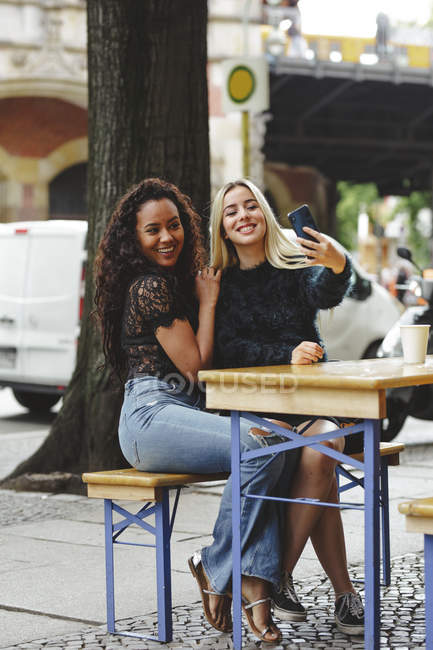 Beautiful young women sitting in Berlin street cafe taking selfie — Stock Photo