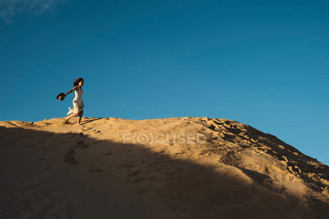 Mulher de vestido branco de pé em distante no sol iluminado colina arenosa em Tarifa, Espanha com céu azul e nuvem branca — Fotografia de Stock