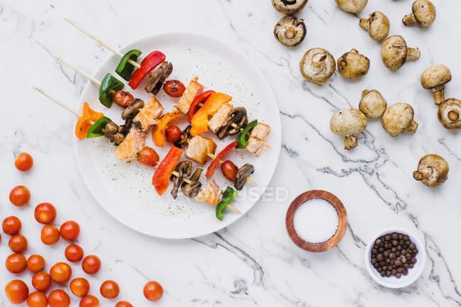 Stücke von Kirschtomaten, Paprika, Lachs und Pilzen an Spießen auf dem Tisch mit Pilzen serviert — Stockfoto
