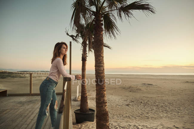 Seitenansicht einer betrachtenden Frau, die sich an Holzgeländer am tropischen Strand lehnt und den Sonnenuntergang in Tarifa genießt, Spanien — Stockfoto