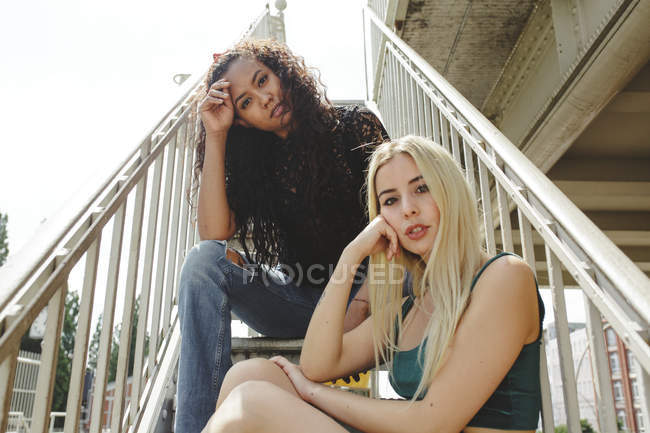 Hermosas mujeres jóvenes sentadas en las escaleras el soleado día de verano en Berlín mirando a la cámara. - foto de stock