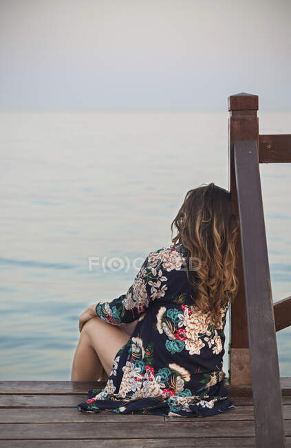 Junge brünette Frau ruht sich auf Dock in der Nähe der Wasseroberfläche aus und blickt auf Küste — Stockfoto