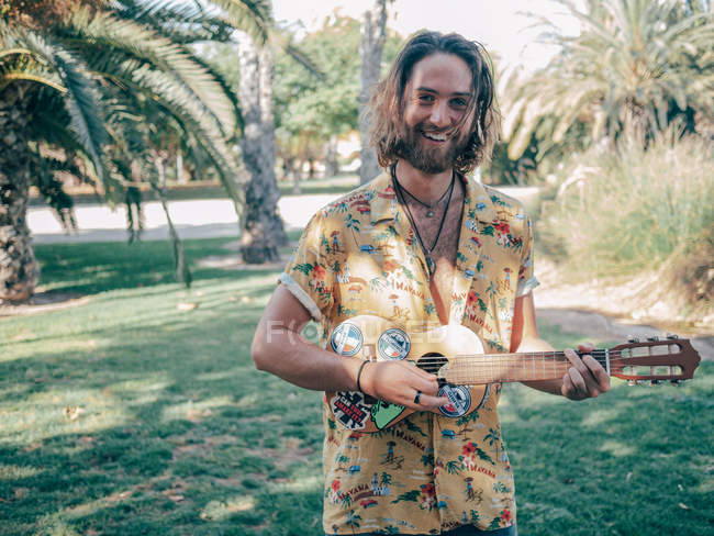 Pensoso barbuto hipster uomo in piedi nella giungla giocare ukulele — Foto stock