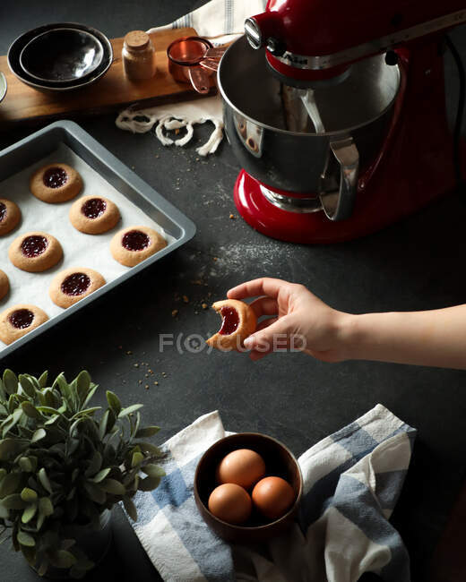Crop person holding bitten cookie over table with ingredients — Stock Photo