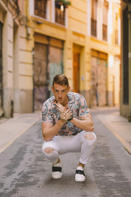 Handsome male in Hawaiian shirt sitting on asphalt on street and looking in camera — Stock Photo
