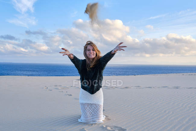 Веселая игривая женщина бросает кучу песка в камеру, сидя на пустой береговой линии в Тарифе, Испания — стоковое фото