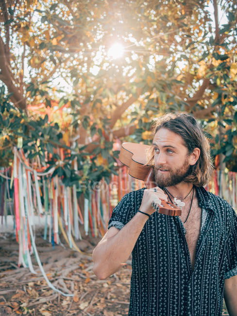 Uomo hipster barbuto pensieroso che viaggia nella giungla con ukulele — Foto stock