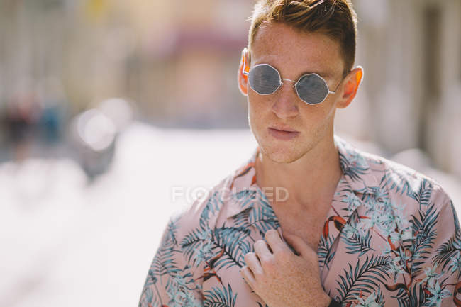 Schöner Mann in hawaiianischem Hemd, der mit Sonnenbrille auf der Straße steht und wegschaut — Stockfoto