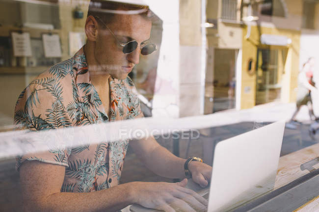 Ragazzo concentrato che lavora su computer portatile a tavola durante finestre in caffetteria — Foto stock