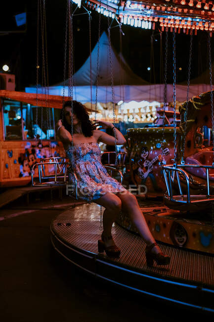 Schöne Frau genießt Fahrt auf Karussell auf Jahrmarkt während Sommerabend auf verschwommenem Hintergrund — Stockfoto