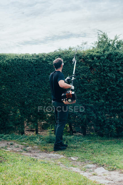 Mann schneidet mit mechanischem Werkzeug eine Arizonica-Hecke — Stockfoto