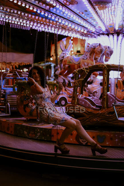 Belle femme appréciant la promenade sur carrousel sur Funfair pendant la soirée d'été sur fond flou — Photo de stock