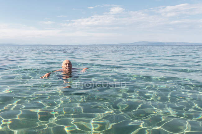 Anciano jubilado flotando en aguas cristalinas disfrutando del clima tropical estando de vacaciones, Grecia - foto de stock