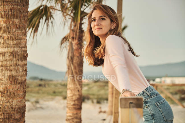 Vista lateral de contemplar a mulher apoiada em grades de madeira na praia tropical desfrutando do pôr do sol em Tarifa, Espanha — Fotografia de Stock