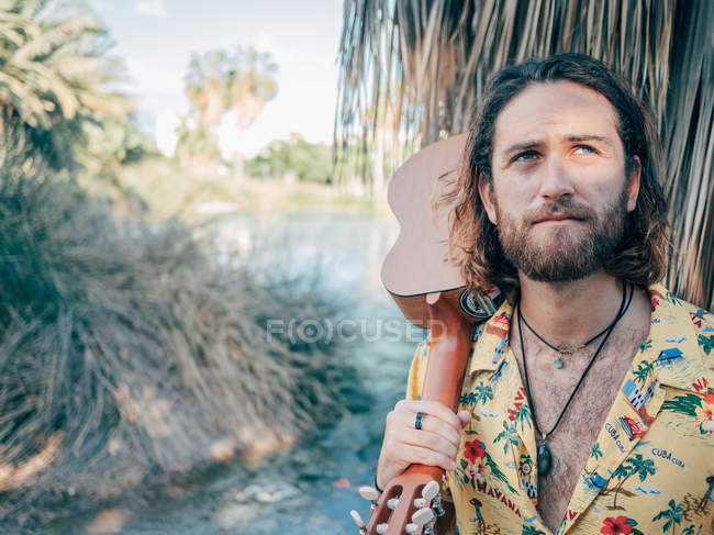 Nachdenklicher bärtiger Hipster-Mann reist mit Ukulele durch den Dschungel — Stockfoto