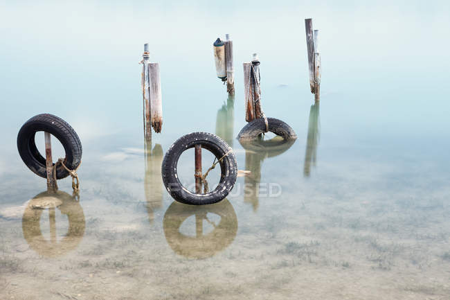 Заброшенные сломанные столбы пирса со старыми черными шинами в кристальной воде в Халкидики — стоковое фото