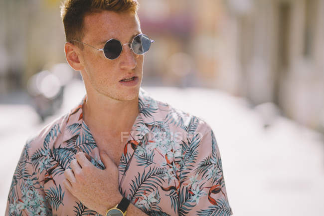 Bonito macho de camisa havaiana em pé na rua com óculos de sol, olhando para longe — Fotografia de Stock