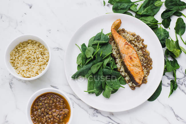 Piatto servito con bistecca di salmone, couscous, lenticchie e verde in tavola con ciotole di lenticchie e couscous — Foto stock