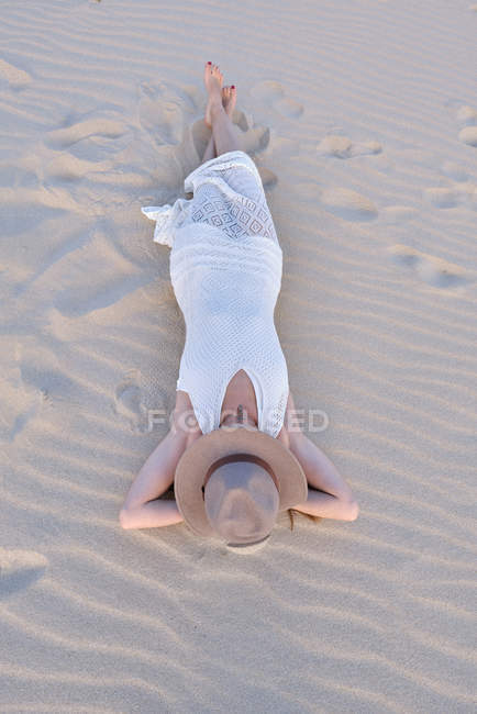 D'en haut femme en robe blanche et chapeau couché sur une plage de sable fin à Tarifa, Espagne — Photo de stock