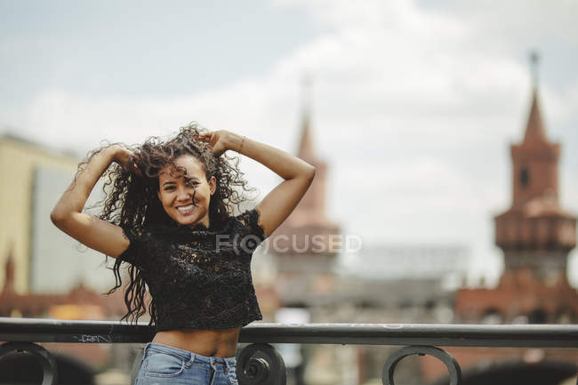 Menina hispânica bonita inclinada em grade no dia de verão em Berlim no fundo borrado olhando para a câmera — Fotografia de Stock