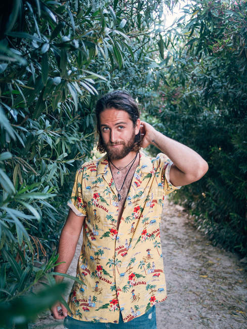 Pensativo guapo barbudo hipster hombre caminando en la selva mirando en cámara - foto de stock