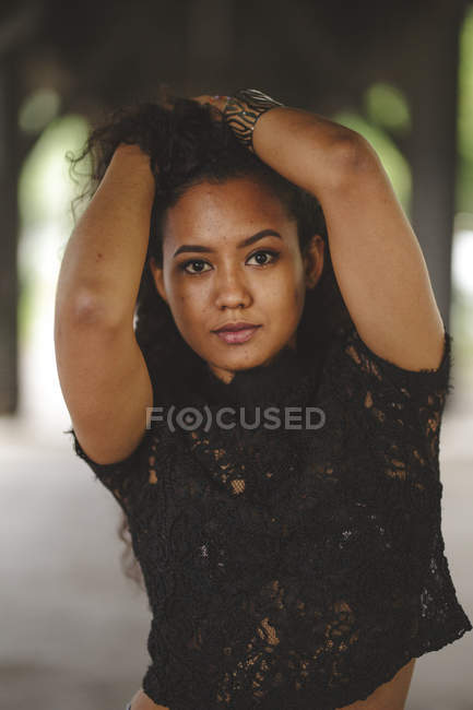 Cheerful hispanic model holding hair in Berlin on blurred background looking at camera — Stock Photo