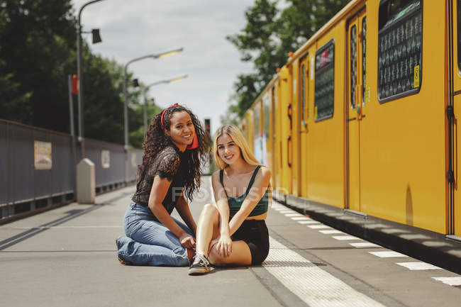 De belles jeunes femmes assises sur le quai d'un train pendant la journée d'été à Berlin regardent la caméra — Photo de stock