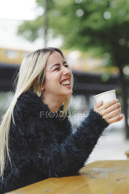 Belle femme gaie buvant du café dans un café de rue à Berlin en milieu urbain flou — Photo de stock