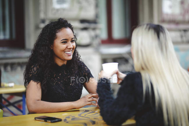 Side view of beautiful young women sitting in Berlin street cafe talking and laughing — Stock Photo