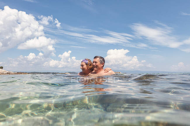 Coppia di uomini e donne anziani che si godono l'acqua dolce mentre nuotano insieme in acqua cristallina nella giornata luminosa, Halkidiki, Grecia — Foto stock