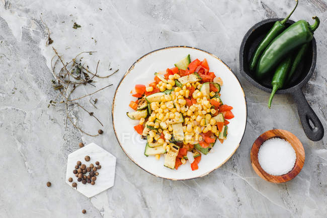 Served bowl with corn and cut tomatoes and zucchini on table with salt and pepper — Stock Photo