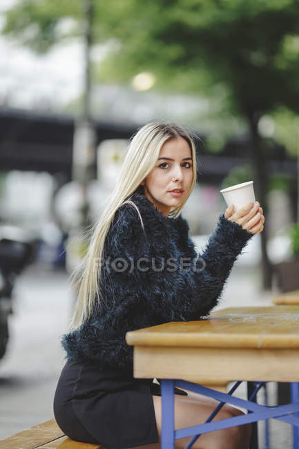 Hermosa mujer alegre bebiendo café en el café de la calle de Berlín sobre fondo urbano borroso. - foto de stock