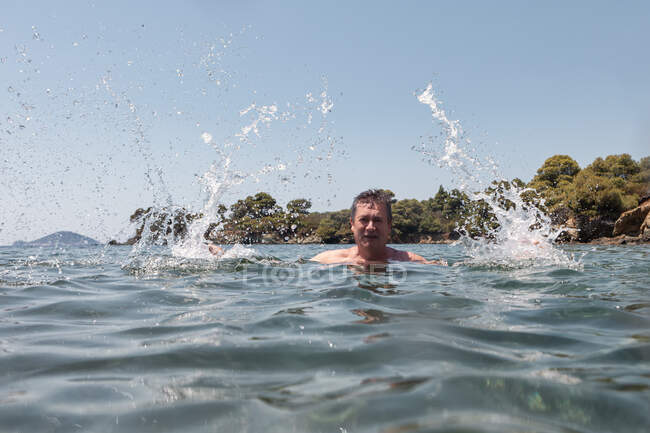 Bald mustache elderly man enjoying and splashing water looking at camera in bright sunny day in Greece Halkidiki — Stock Photo