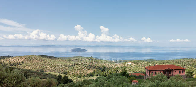 Vista panorámica de la costa verde con villa roja y plantación verde en la orilla contra el mar de cristal a la luz del sol, Grecia - foto de stock
