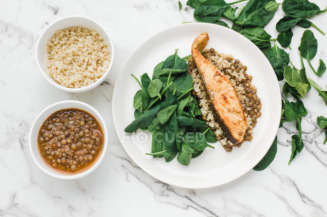 Piatto servito con bistecca di salmone, couscous, lenticchie e verde in tavola con ciotole di fagioli e couscous — Foto stock