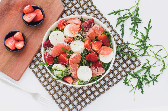 Top view of bowls with strawberries, grapefruit and rocket salad on table served on board — Stock Photo