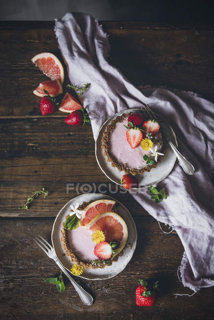Vista superior de deliciosos pasteles de fresa y cítricos servidos en mesa de madera decorada - foto de stock