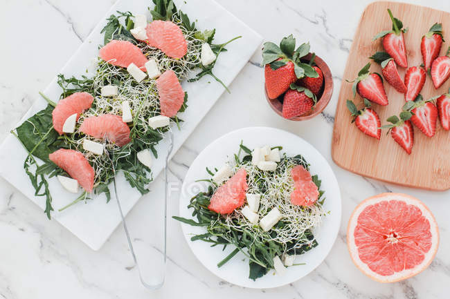 Top view of bowls with strawberries, grapefruit and rocket salad on table served on kitchen boards — Stock Photo