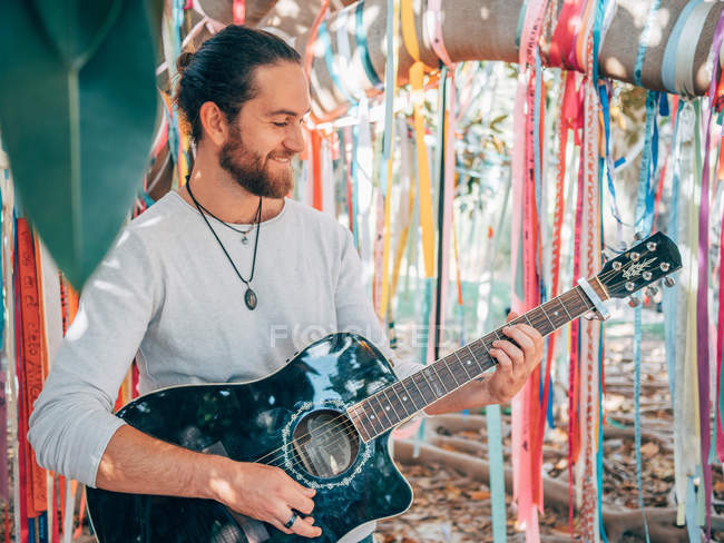 Bärtiger Hipster-Mann spielt im Sommer Akustikgitarre unter geschmücktem Baum — Stockfoto