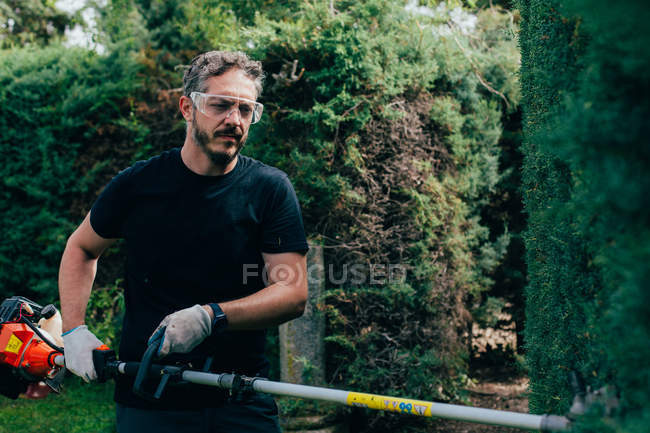 Кавказский человек обрезает изгородь из оризоники механическими инструментами — стоковое фото