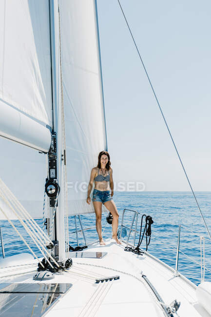 Путешествующая женщина в купальнике, стоящая на борту яхты в море и смотрящая в сторону — стоковое фото
