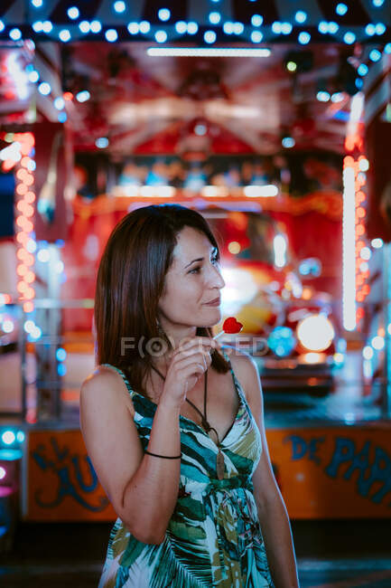 Mulher com pirulito no parque de diversões na noite quente de verão no fundo borrado — Fotografia de Stock