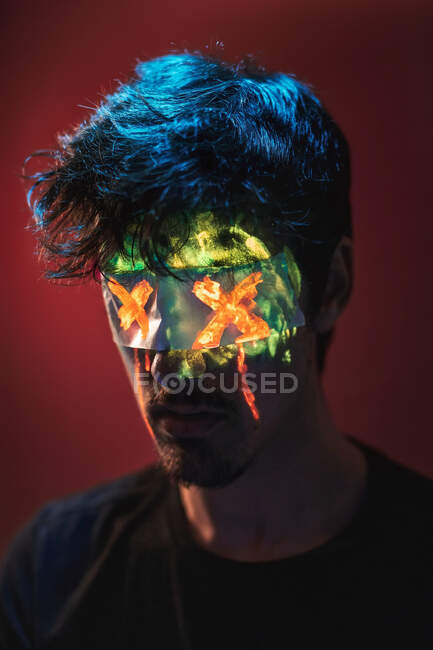 Homme aux cheveux bleus et au visage vert rayonnant portant du ruban adhésif peint en X sur fond rouge — Photo de stock