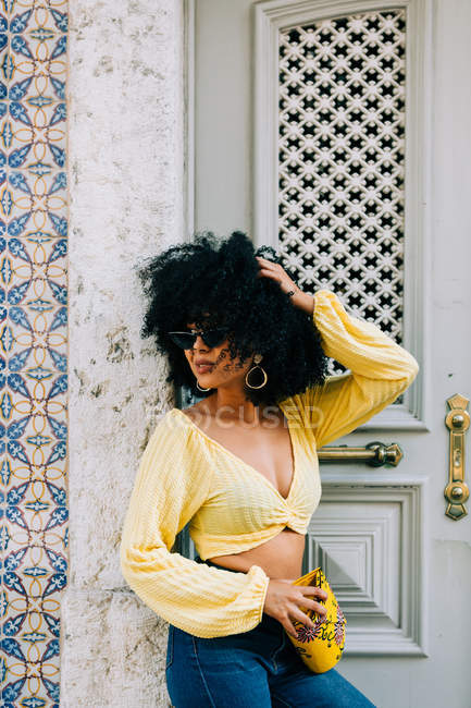 Femme afro-américaine à la mode en haut de culture jaune et jeans debout à la porte et regardant loin — Photo de stock
