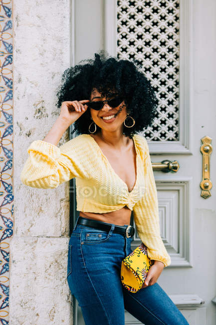 Модний афроамериканець жінка в жовтій верхній частині врожаю і джинси стоячи на дверях і дивлячись на камеру — стокове фото