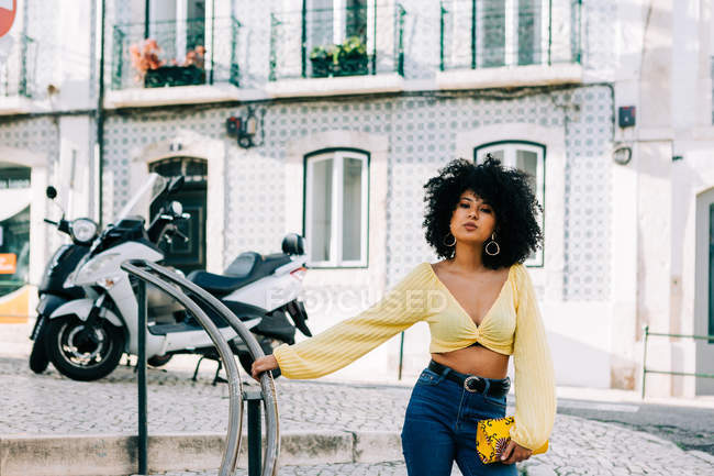Fashionable African American woman in crop top and jeans leaning on railing — Stock Photo