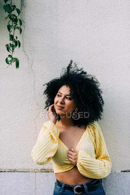 Hübsche ethnische Frau in gelbem Crop Top mit schwarzem lockigem Haar, die auf der Straße wegschaut — Stockfoto